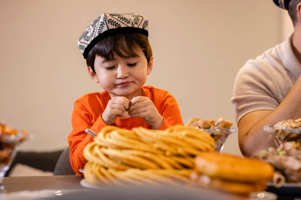 Portrait of smiling middle eastern boy sitting at dining table. Arab male is wearing thawb. He is looking at camera.
