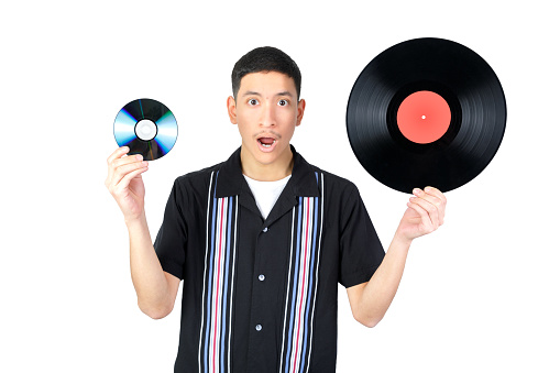 Surprised guy holding a vinyl record and a CD. Looking at camera opening the mouth. Isolated on white background. 18-20 years old latin american guy.
