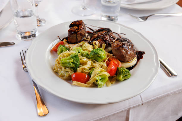 Beef chops on goat cheese seasoned with balsamic vinegar, served with tagliattele pasta, broccoli and tomato, ethnic restaurant serving Mediterranean specialties