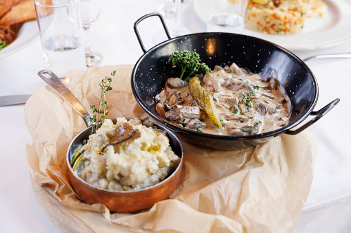 Veal medallions in mushroom gravy in pan, mashed potatoes with truffle slices as side served on restaurant table, ethnic restaurant serving Balkans' and Mediterranean specialties