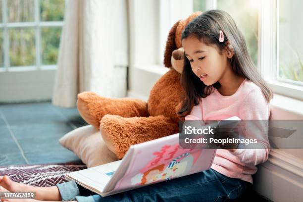 Shot Of A Little Girl Reading A Book At Home Stock Photo - Download Image Now - Child, Reading, Book