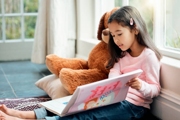 ujęcie małej dziewczynki czytającej książkę w domu - czytanie zdjęcia i obrazy z banku zdjęć