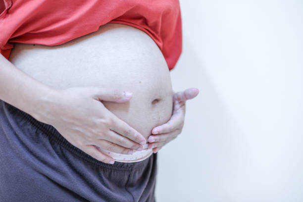 Close-up of pregnant woman holding belly in house