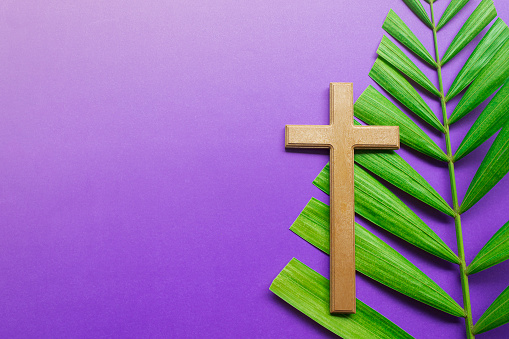 Good Friday, Palm Sunday, Ash Wednesday, Lent Season and Holy Week concept. Cross and palm leaves on purple background.