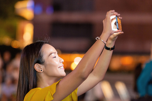 Profile view of a woman smiling as she records a video of an event using her smartphone.