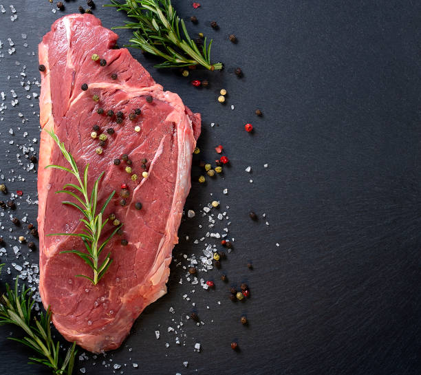 istock Raw beef steak with rosemary and spices on black background. 1377710532