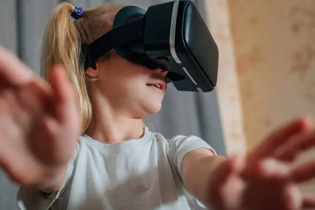Photo of child girl at home in virtual reality VR glasses watching video, playing games. modern children are well versed in technological innovations. generation alpha