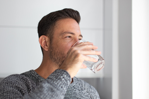 Man drink water from glass indoors, looking away