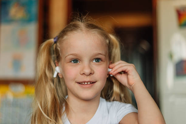 ritratto di un bambino sorridente, ascoltando musica in cuffie bianche, ballando, scherzando a casa. bella ragazza ascolta una fiaba audio in cuffia. generazione alfa - one kid only audio foto e immagini stock