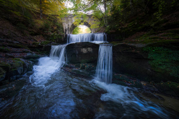 Beautiful landscape of gorgeous waterfall in the woods, and ancient roman bridge crossing over it.
