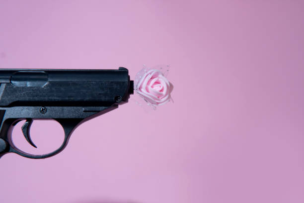 istock Black gun shoots a pink rose on a pink background .Peace, unification, harmony, no violence, spreading love concept 1377784827