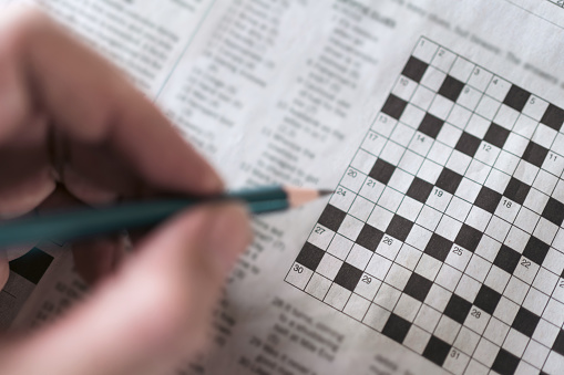 Close up hand holding pencil over crossword puzzle on newspaper. Game on for writing some letters to solve and completing the empty table.