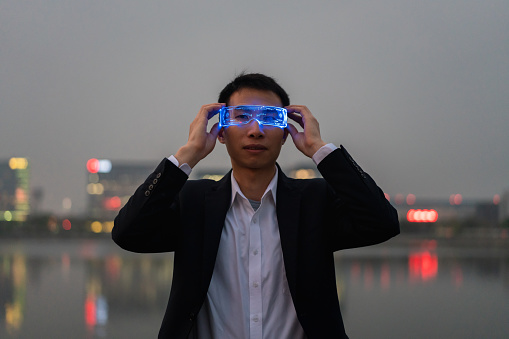 Asian male white collar wearing smart glasses on the background of city night lights