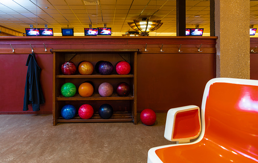 Wooden rack of multi-coloured bowling balls in a retro bowling alley.