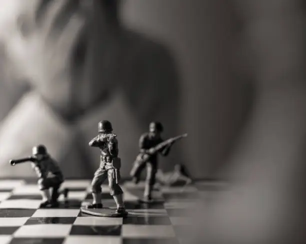 Photo of Black and white image with soldier figurines standing on a chessboard,Blurred chess player with hands on his face disappointed that he lost the game,