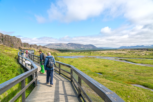 Reykjavik, Iceland - July 20, 2021: Group of tourists  walking on wooden footpath. Thingvellir national park, very important for Icelanders, as it was site of the national parliament in the past. The area is located on the Mid-Atlantic ridge, where the continents of Europe and America drift apart causing earthquakes and volcanic activity.