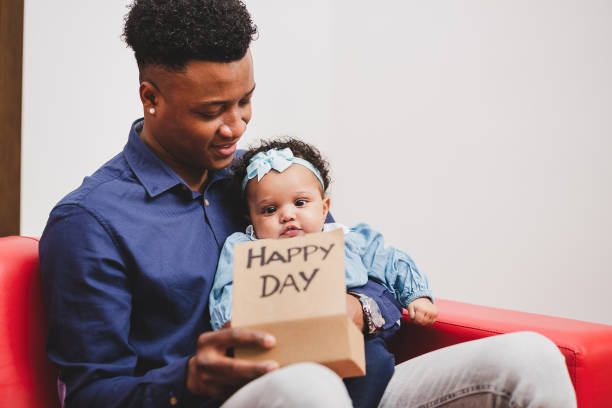 Afroamerican father and his daughter with a gift in a red couch.