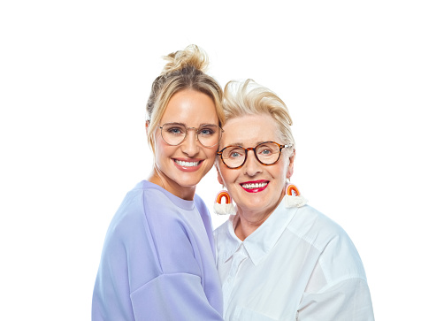 Portrait of smiling daughter and mother embracing against white background.