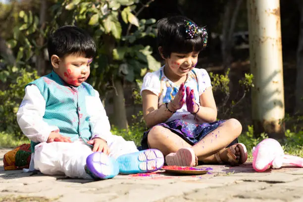 Photo of Happy Asian Indian Kids Boy And Girl Enjoying The Festival Of Colors With Holi Color Powder Called Gulal Or Rang
