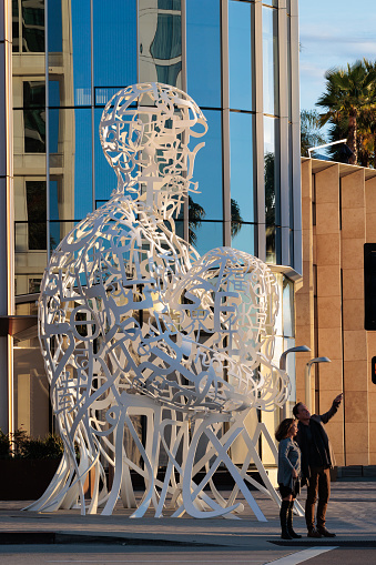 The Pacific Soul Sculpture in downtown San Diego, California. A couple stands at the street corner. The man is pointing into the distance.