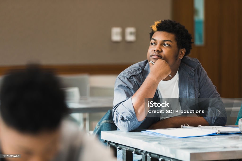 Teen boy rests chin on hand and daydreams in class The teenage boy rests his chin on his hand as he looks away and daydreams during class. Boredom Stock Photo