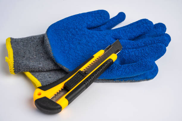 blue rubberized work gloves and a stationery knife lie on a white background stock photo