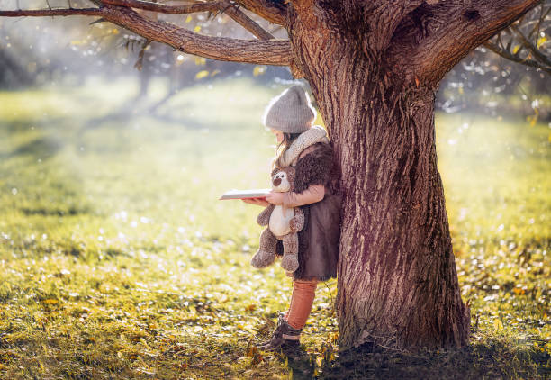 A child reads a book with his teddy bear in the forest, leaning against a tree, fabulous photo.