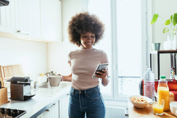 istock African American woman using smart phone in kitchen and preparing coffee from coffee machine 1378117857