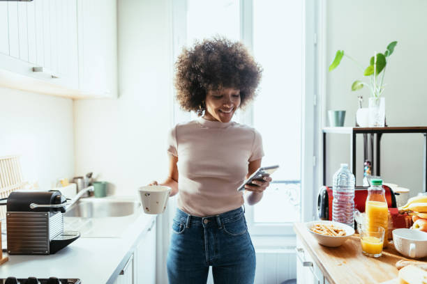 istock African American woman using smart phone in kitchen and preparing coffee from coffee machine 1378118921