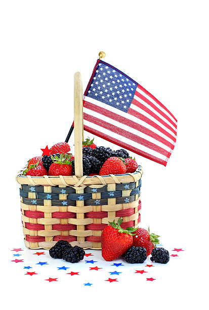 Patriotic basket full of fresh strawberries and blackberries.  Stars and a flag surround basket which is on white with copy space.