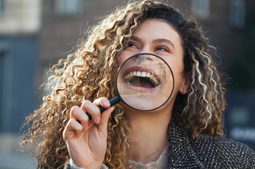 Young woman holding magnifying glass in front of her smile