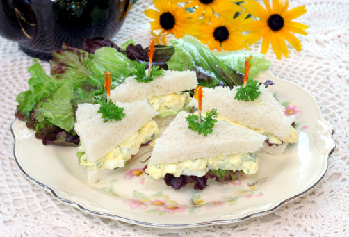 Dainty egg salad tea sandwiches on a vintage plate and doily.