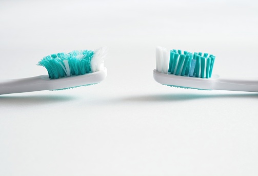 Comparison between a brand new and worn out toothbrush ready for replacement. Aqua colored toothbrushes one new one old on a white background with copy space.