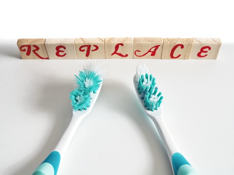 An old worn out toothbrush next to a fresh new one with the word replace in block letters in the background, a hygiene concept comparison. Two toothbrushes on white background with toy blocks in the background with red letters warning of the need for replacement.