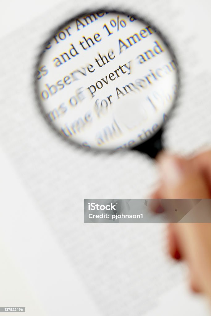 Poverty Hand holding maginfying glass focusing on poverty. Focus - Concept Stock Photo