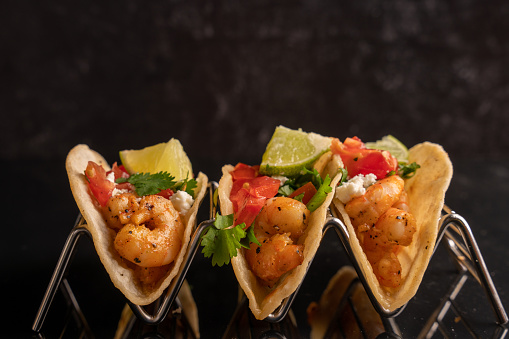 Shrimp Street Tacos on a black reflective background. Ready to be eaten tacos with lime and other toppings.