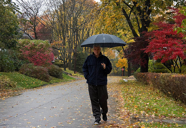 man walking down country road in autumn rain stock photo