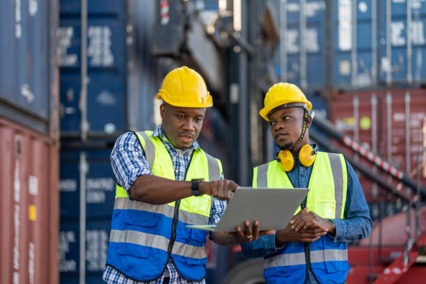 afrikanische arbeiter, ingenieur, techniker mit laptop zur überprüfung und inspektion des containerbereichs vor ort für den schiffstransport und das heben von maschinen. konzept menschen betrieb in der schwerindustrie. - harbor commercial dock engineer service stock-fotos und bilder