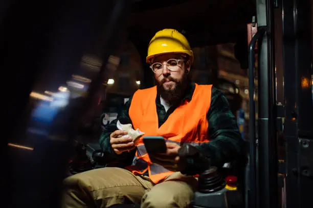 Worker looks at the phone while he has a sandwich in his other hand