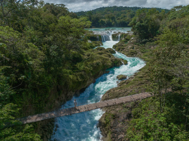 vue aérienne d’une femme marchant sur un pont suspendu au-dessus de la cascade de las nubes au chiapas - horizon over water white green blue photos et images de collection