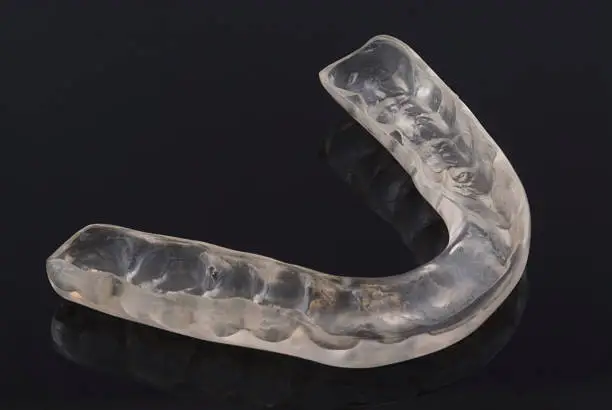 Clear mouthguard for the teeth of the top jaw, made out of dental polymer on the dark background. It covers the teeth and usually used during night time to protect them against tooth clenching.