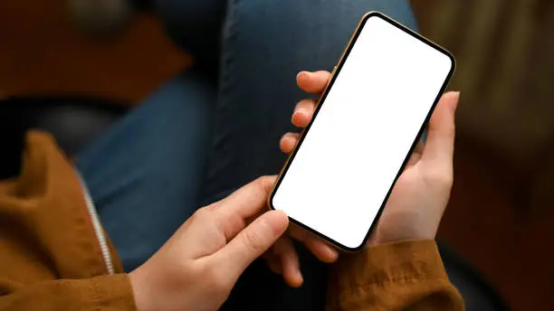 Close-up, focus hands, Female in casual outfit, sits and relaxes at living room, using smartphone. phone white screen mockup.