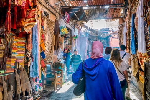 Marrakech, Morocco - October 19, 2015. Early morning in the city souk, as pedestrians walk on a narrow street past shops selling tourist merchandise and dry goods.