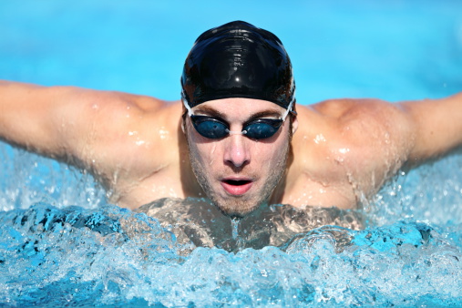 Swimmer. Man swimming butterfly strokes in competition. Competitive male sport swimmer wearing swimming goggles and cap. Young caucasian male fitness model.