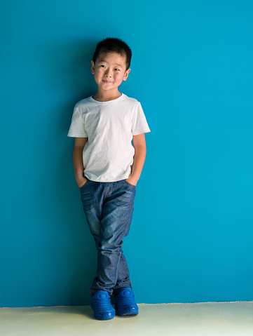 A cute boy standing in front of the blue wall.