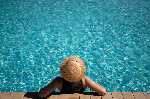 young beautiful unrecognizable woman in a straw hat is resting during a vacation in the pool. copy space.