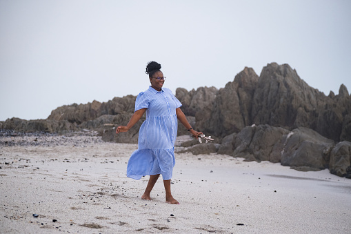 An African woman in a blue dress enjoys a walk on the beach