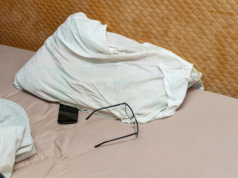 unmade bed, mobile phone under pillow and spectacles, indoor shot