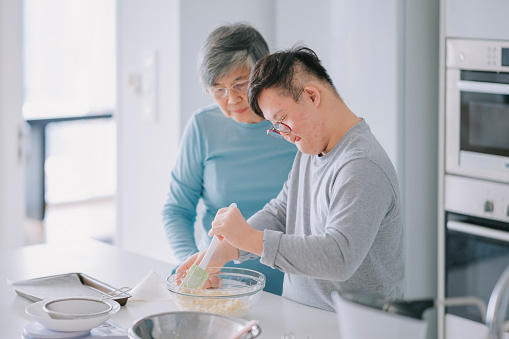 Asian Chinese disability down syndrome grandson learning from his grandmother preparing cake in kitchen