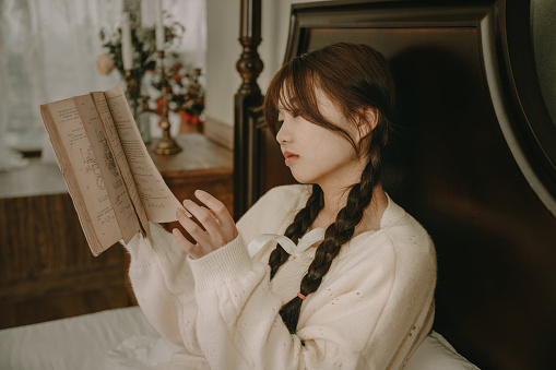 A beautiful asian girl reading in bed
